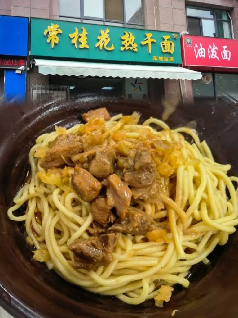 许昌东城区常桂花热干面店门口，蓝色招牌清晰可见，一碗拌匀的热干面近景