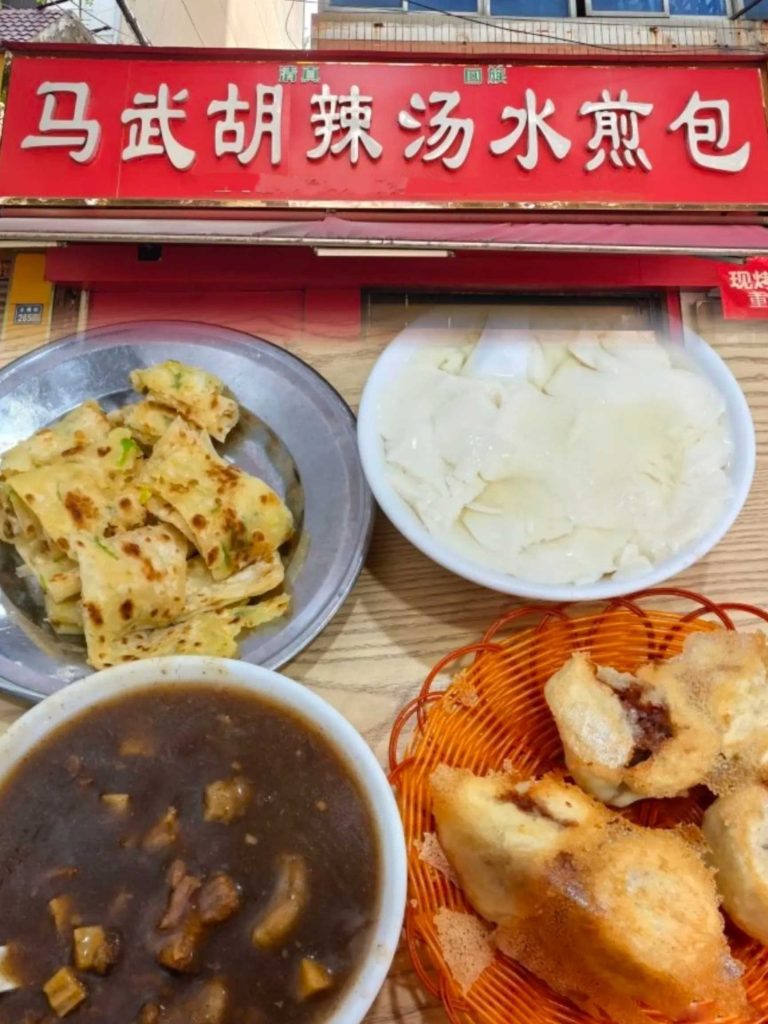 许昌古槐街老城区“马武胡辣汤海三水煎包”店面，红底黄字招牌，桌上摆着胡辣汤和水煎包