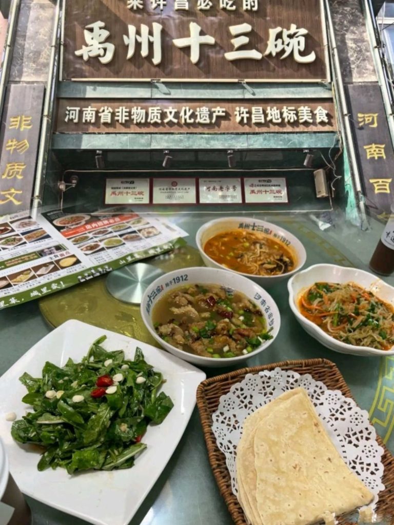 许昌建安大道“禹州十三碗”餐厅门头，黑色牌匾金色大字，桌上一套完整宴席菜品